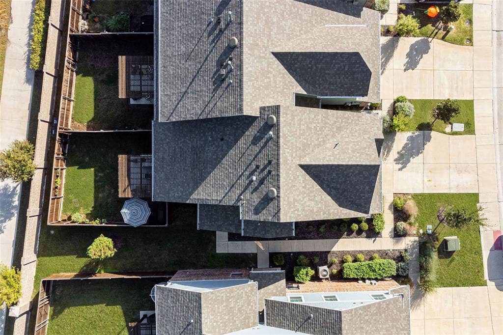 Aerial view featuring a multi-pitched composition shingle roof, concrete driveway, and enclosed backyard spaces with wood fencing