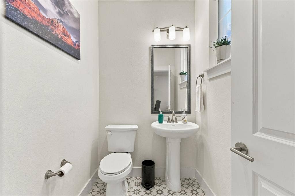 Powder room featuring a pedestal sink, framed wall-mounted mirror, three-light fixture, and patterned floor tile