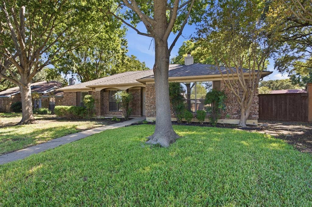 661 Thompson Drive, Coppell, TX 75019 Mature shade trees frame this expansive lawn with concrete walkways, brick exterior construction, and covered porch areas with beam detailing