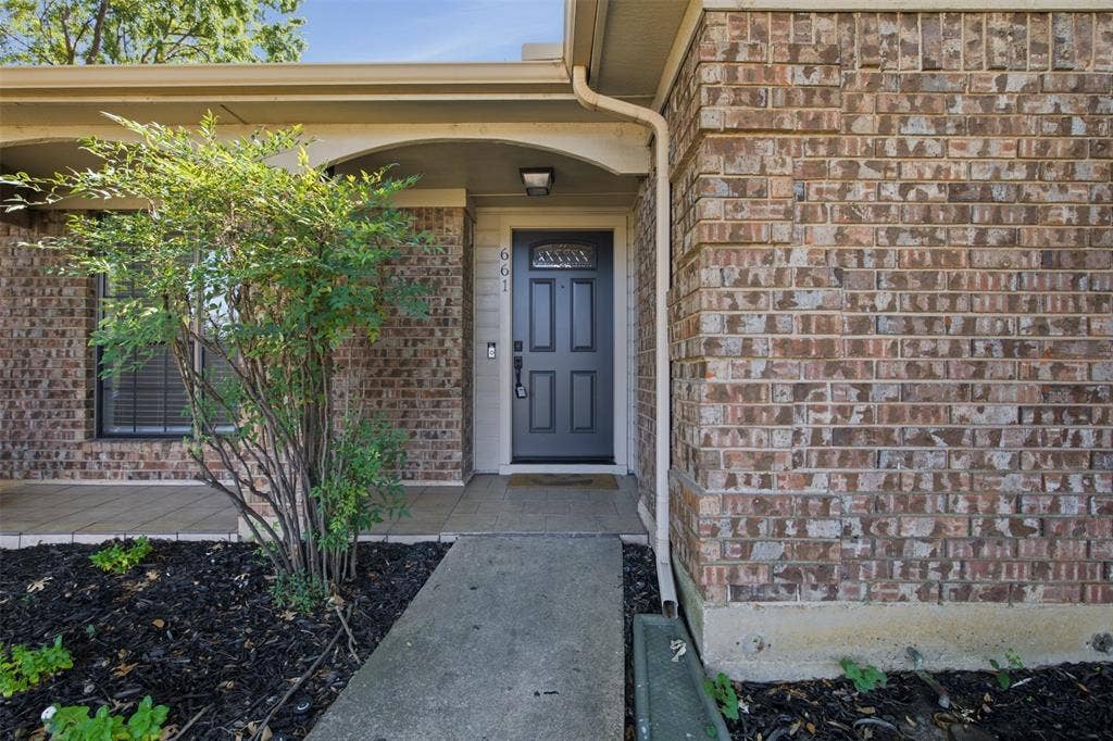 661 Thompson Drive, Coppell, TX 75019 Brick exterior facade with a dark-paneled entry door, arched entryway, and covered front porch