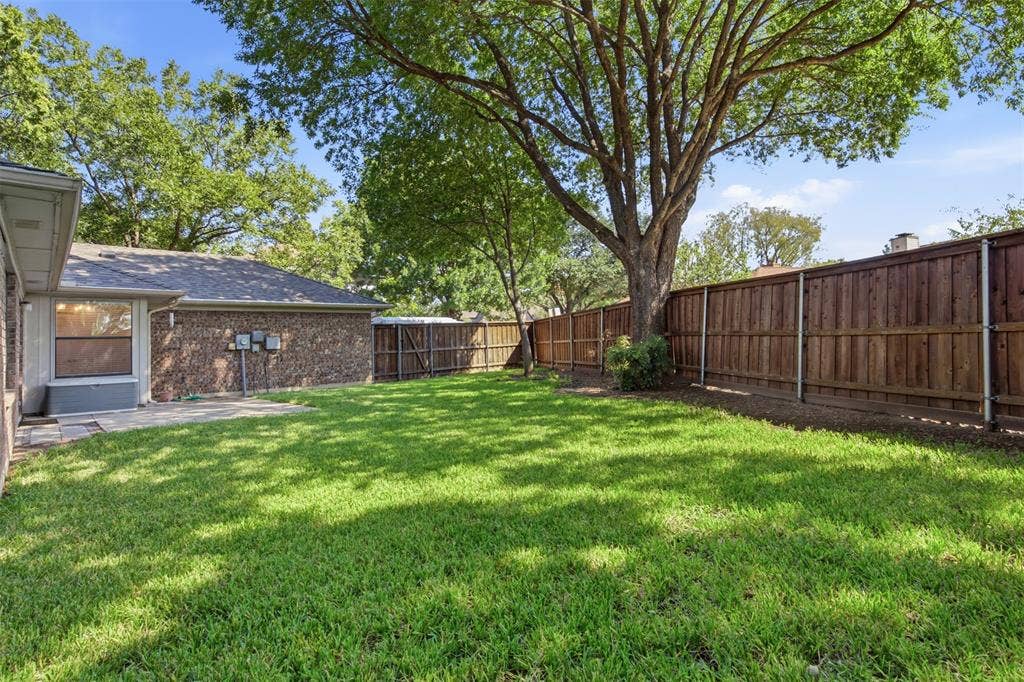 661 Thompson Drive, Coppell, TX 75019 Expansive green lawn with a mature tree, stone patio, and a wood privacy fence