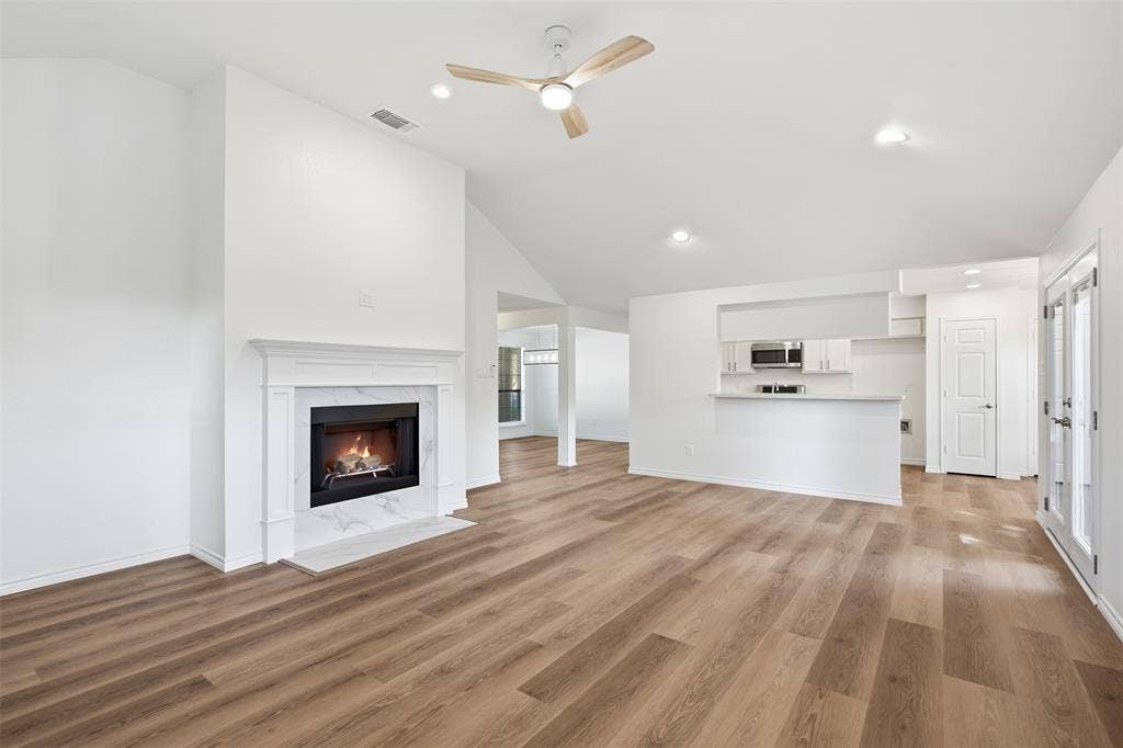 661 Thompson Drive, Coppell, TX 75019 Vaulted ceiling with a ceiling fan, fireplace with a marble-look surround, wood-finish flooring, kitchen pass-through with white cabinetry, and double glass doors