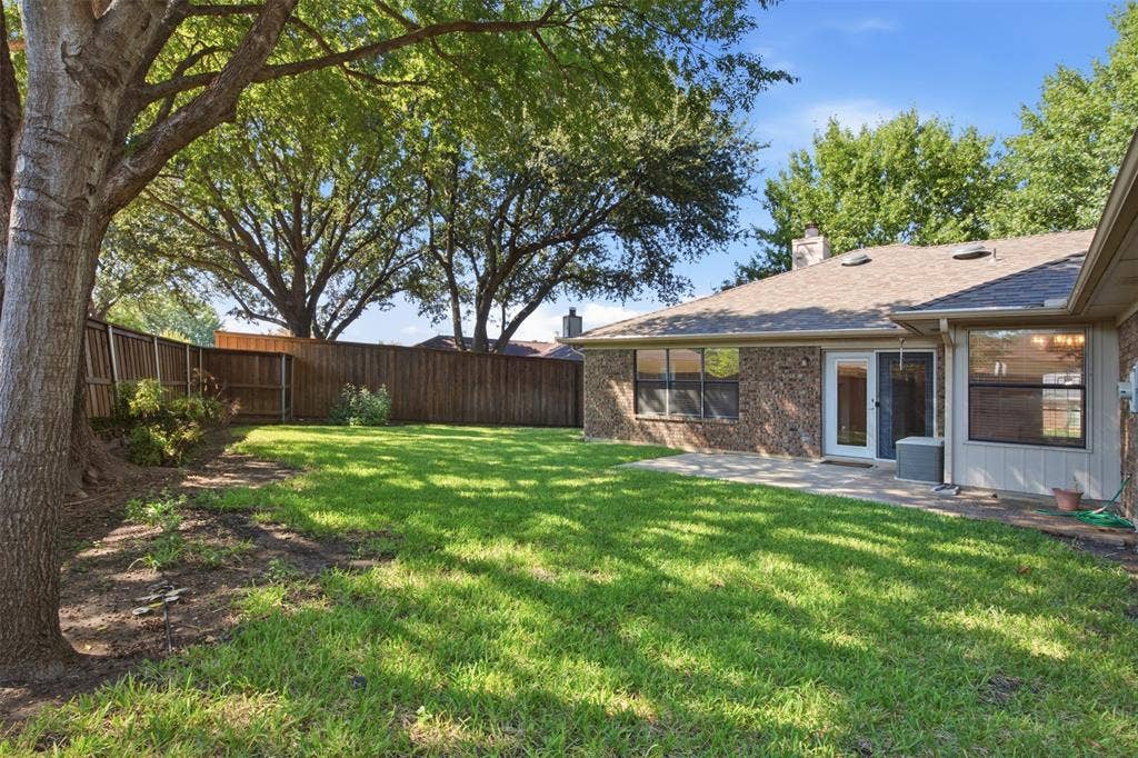 661 Thompson Drive, Coppell, TX 75019 Expansive green lawn with mature trees, a privacy fence, and a patio area