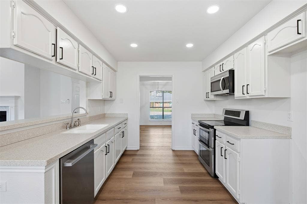 661 Thompson Drive, Coppell, TX 75019 Galley kitchen featuring white cabinetry with brushed nickel hardware, stainless steel appliances including a double wall oven and built-in microwave, quartz countertops, and wood-finish flooring throughout