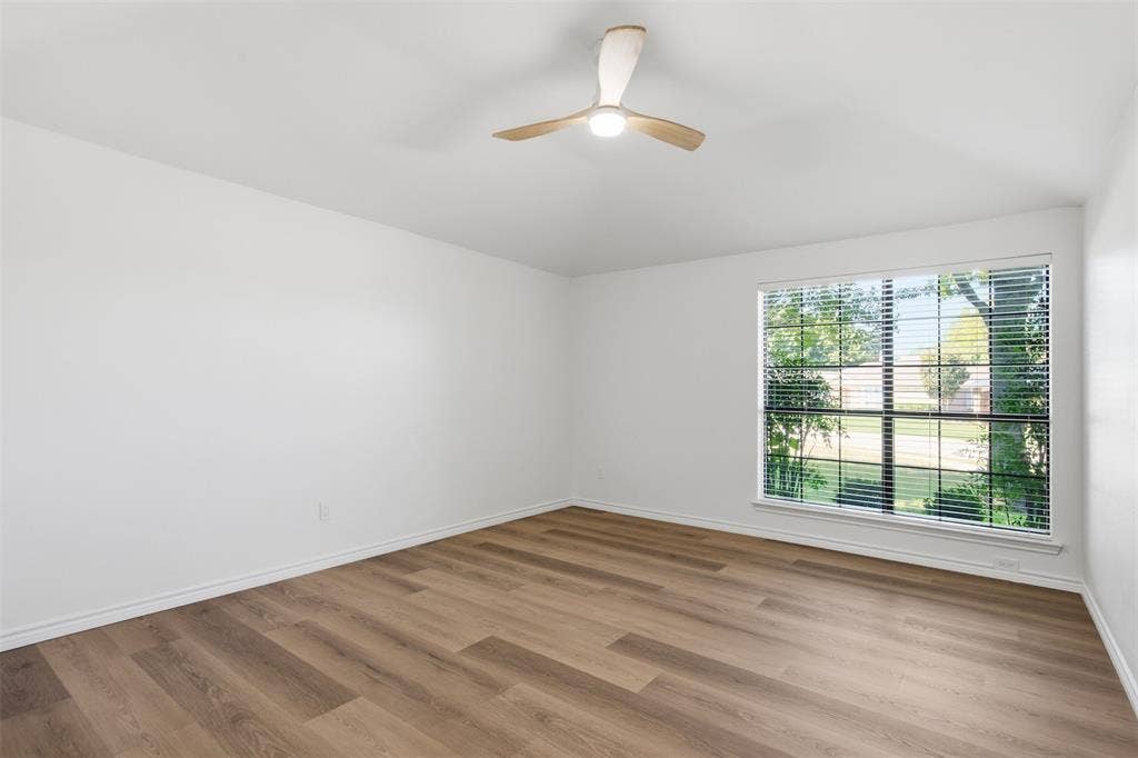 661 Thompson Drive, Coppell, TX 75019 Bright corner bedroom featuring wood-finish plank flooring, abundant natural light from expansive multi-pane windows, and a modern ceiling fan with integrated lighting