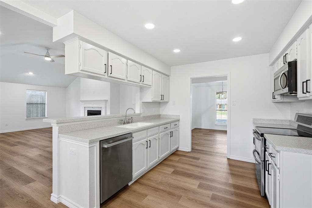 661 Thompson Drive, Coppell, TX 75019 Open-concept kitchen with white cabinetry, stainless steel appliances, wood-finish flooring, and recessed lighting