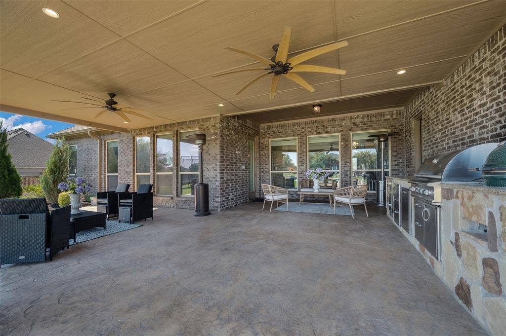 Covered patio featuring stamped concrete flooring, a full brick exterior, a built-in outdoor kitchen with stone veneer, and dual ceiling fans with recessed lighting