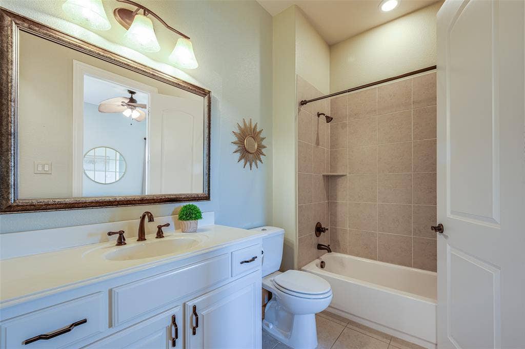 Bathroom featuring a white vanity cabinet, solid-surface countertop with an integrated basin, bronze-finish hardware, a full-width mirror with a decorative frame, and a tub-shower combination with tiled surround