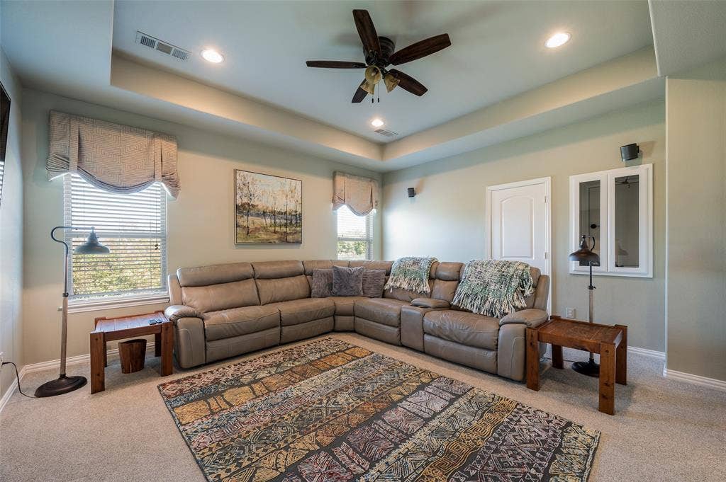 Tray ceiling with recessed lighting and a central ceiling fan, neutral wall tones, and windows featuring window treatments