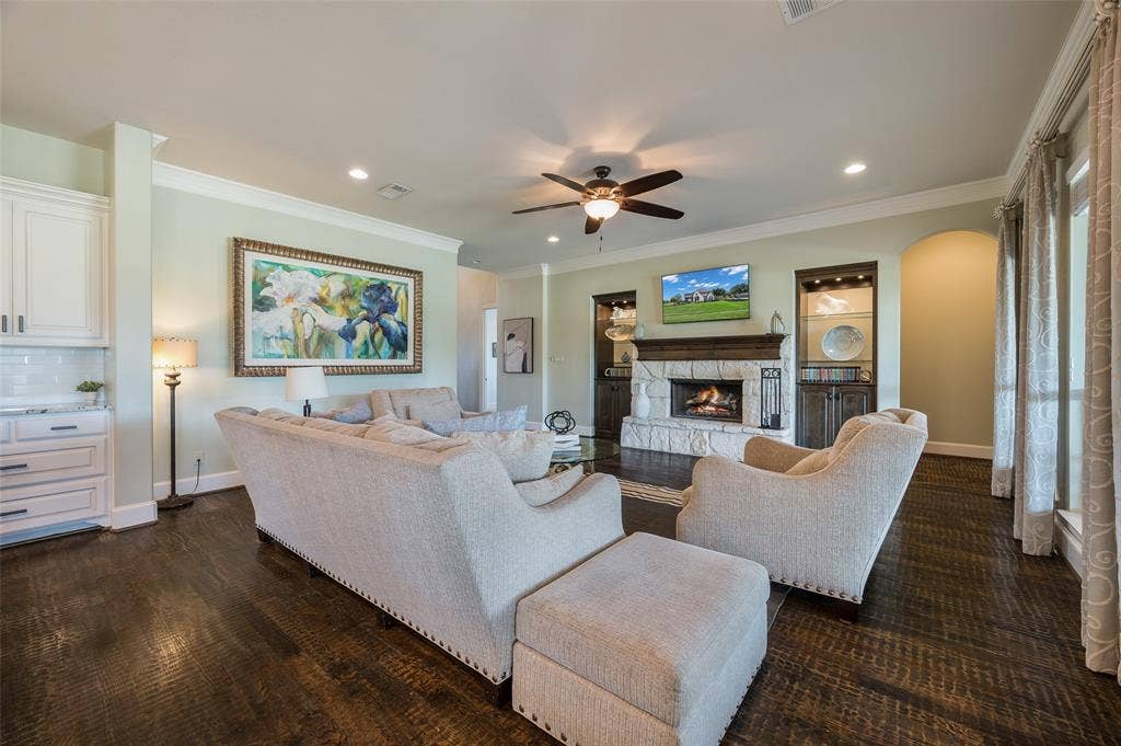 Living area featuring dark wood-finish flooring, a stone-faced fireplace with a wood mantel, built-in cabinetry, and crown molding