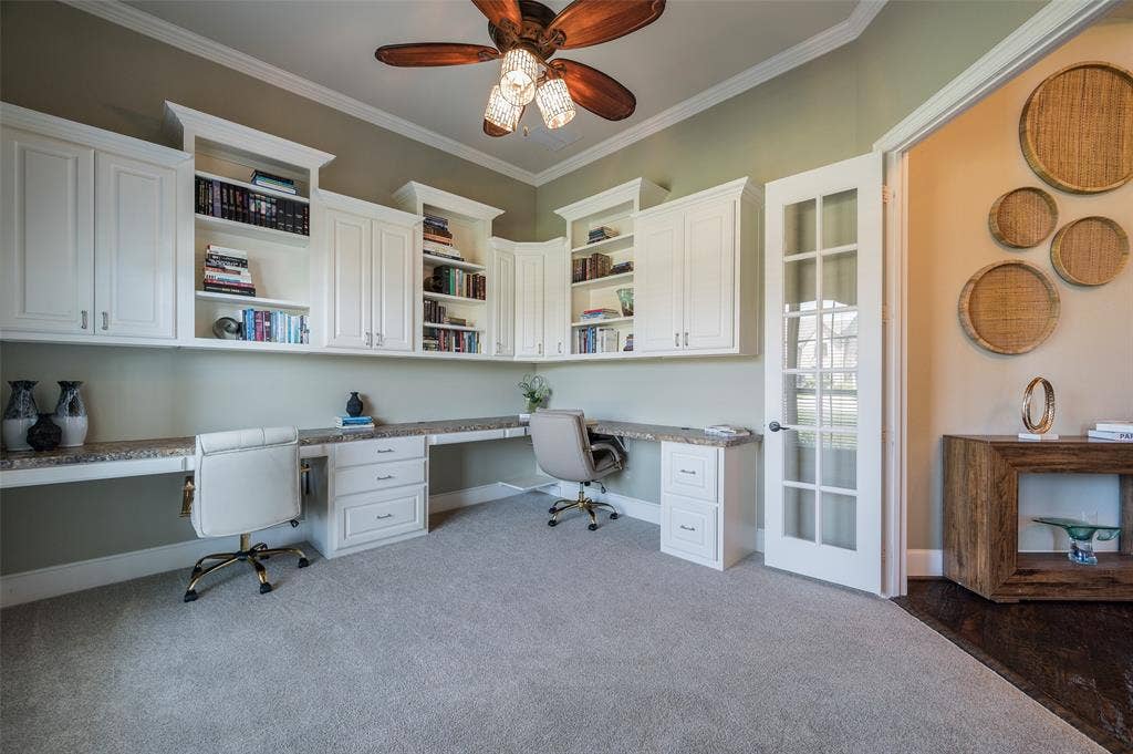 Built-in white cabinetry with integrated shelving, extended stone-surface desktop, ceiling-mounted paddle fan, and glass-paneled entry door