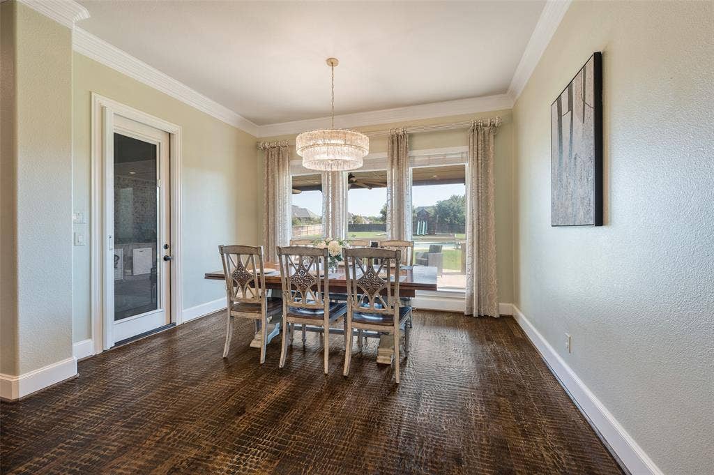 Dining area featuring wood-finish flooring, crown molding, a multi-tiered crystal drum chandelier, and a single-light glass panel door