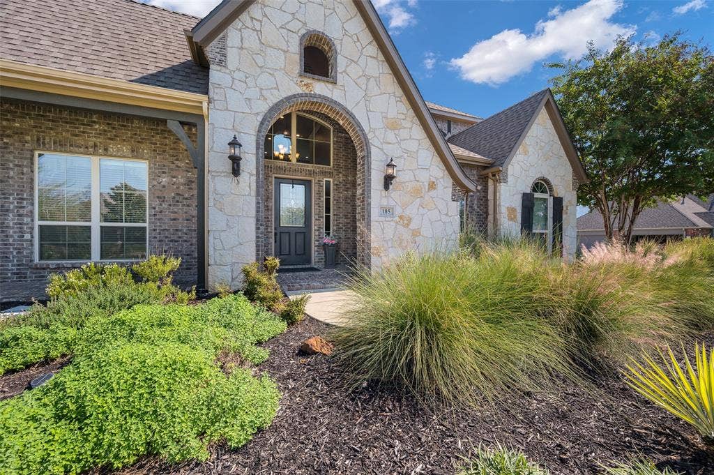 Exterior facade featuring a combination of brick and cut-stone masonry, an arched entryway, shingled roofing, and a front-facing decorative glass paneled door