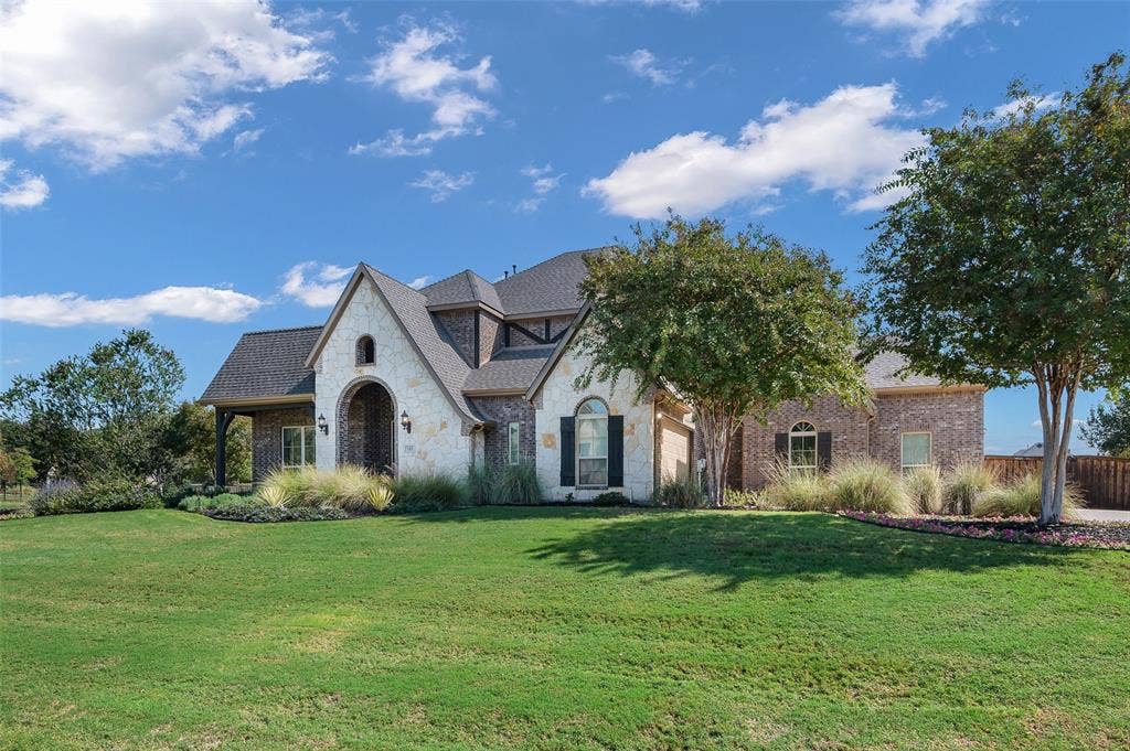 Multi-gabled exterior featuring a blend of light stone and brick masonry, high-pitched shingle roofing, arched entryway, and dark-framed windows with exterior shutters