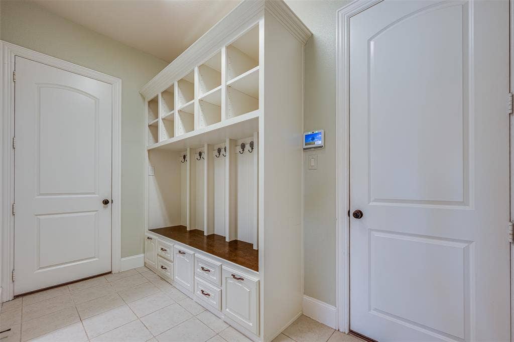 Built-in floor-to-ceiling cabinetry featuring overhead cubbies, integrated coat hooks, lower drawers, and a wood-finish bench surface, paired with ceramic tile flooring and two paneled interior doors
