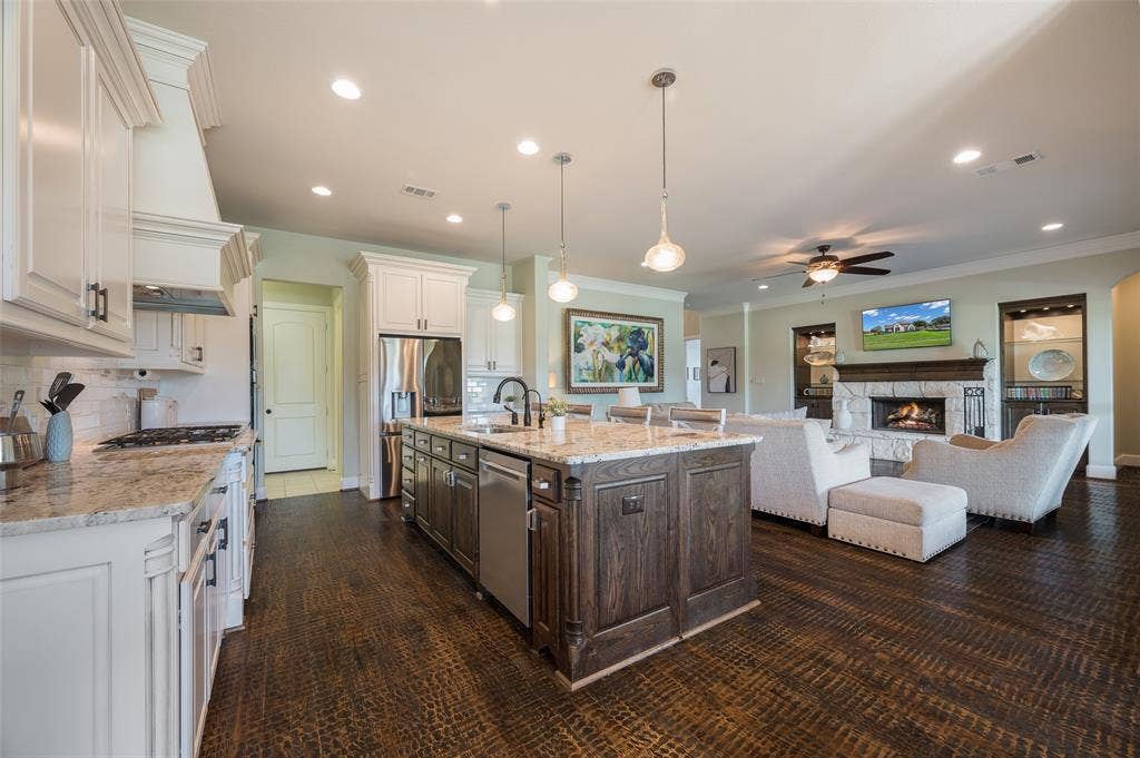 Kitchen featuring white shaker-style cabinetry, dark-stained wood kitchen island, stone-finish countertops, stainless steel appliances, and wood-finish flooring