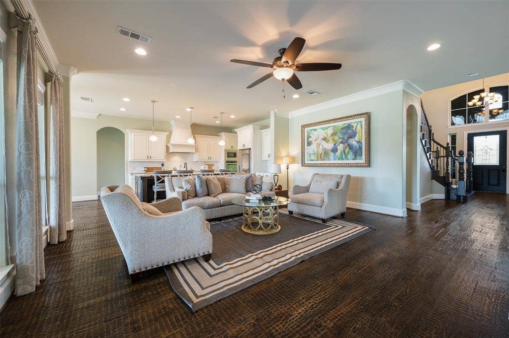 Open-concept interior featuring dark-stained wood-finish flooring, recessed lighting, crown molding, a kitchen with white cabinetry and a center island, and a staircase with wrought iron balusters