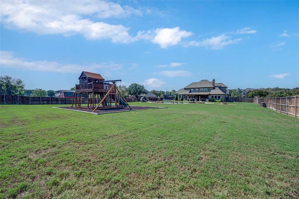 Expansive backyard featuring a large grass lawn, perimeter wood fencing, and a built-in wooden play structure