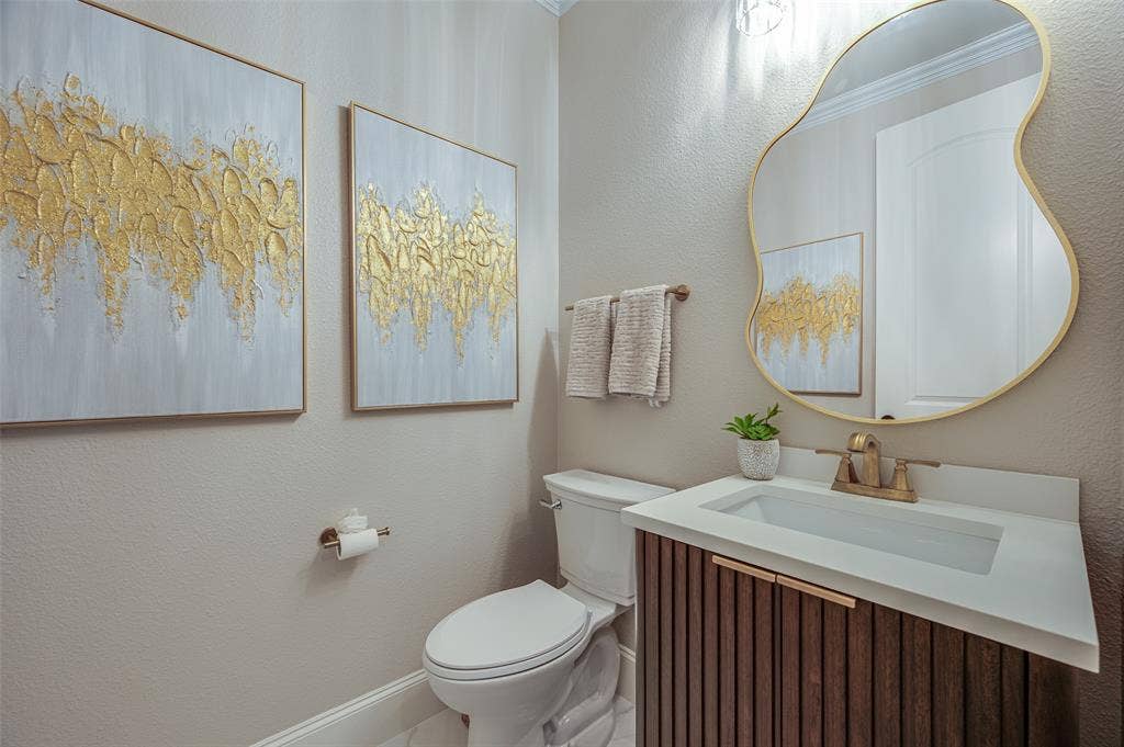 Powder room featuring a fluted wood-finish vanity with a rectangular basin, quartz countertop, organic-shaped mirror with a metallic frame, and wall-mounted brass-finish faucet