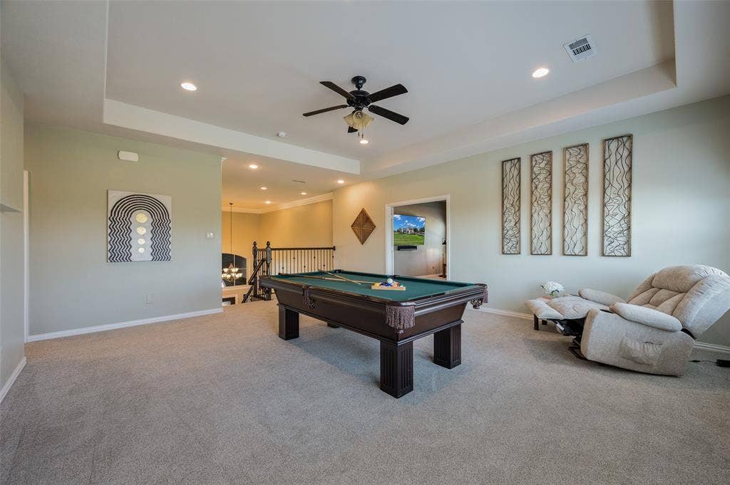 Spacious room featuring a tray ceiling, recessed lighting, a central ceiling fan, and metal spindle stair railing