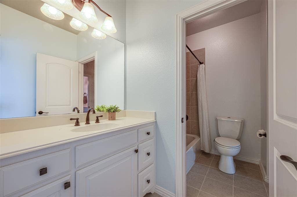 White vanity with stone-style countertop and an integrated oval sink, paired with a large wall-mounted mirror, four-light vanity fixture, and tiled flooring