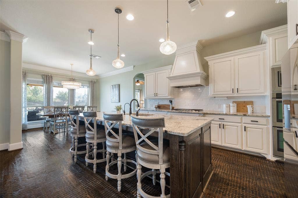 Kitchen featuring white shaker-style cabinetry, stone countertops, a dual-toned center island with pendant lighting, a subway tile backsplash, and dark wood-finish flooring
