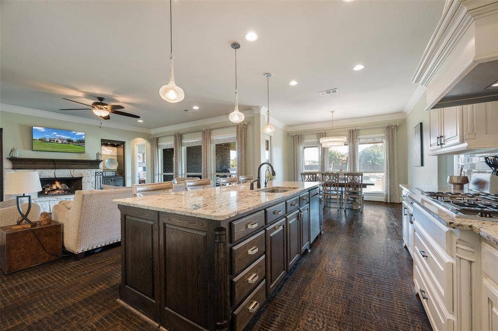Kitchen island with stone countertop, dark-finish cabinetry, wood-finish flooring, recessed lighting, and stone-faced fireplace