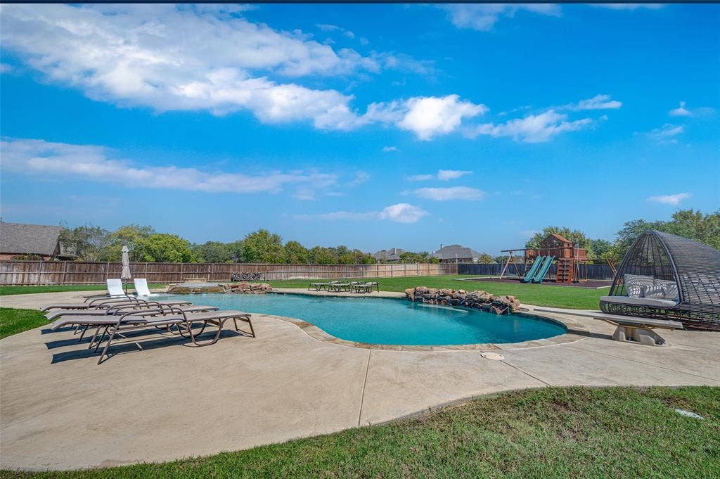 Inground swimming pool with natural stone water features, concrete decking, expansive lawn, and wood privacy fencing