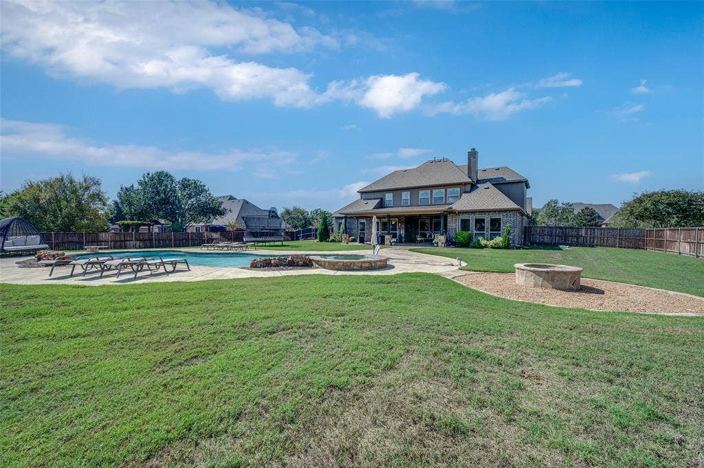 Backyard featuring a swimming pool, integrated stone fire pit, extensive stone patio, and perimeter wood fencing