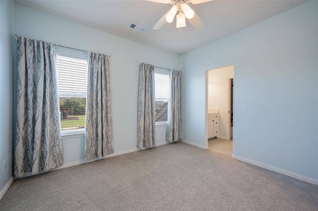 Neutral-toned interior featuring wall-to-wall carpeting, two windows with horizontal blinds, and a multi-bulb ceiling fan