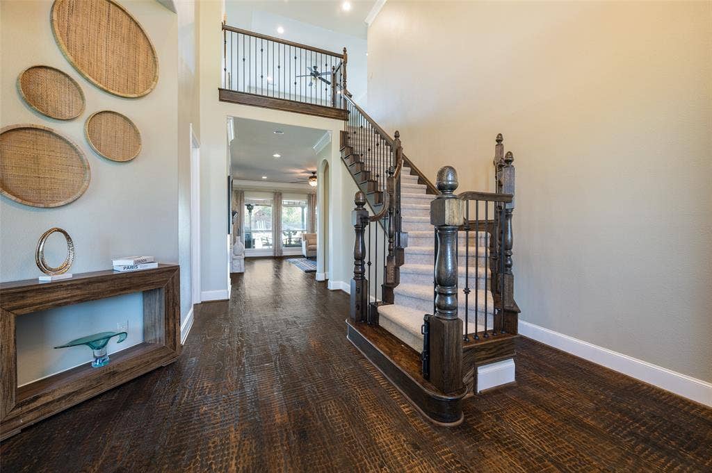 Grand foyer featuring expansive two-story ceilings, wood-finish flooring, and a central staircase with a decorative wood handrail and iron balusters
