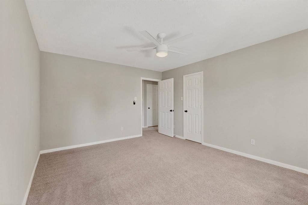Neutral-toned walls, carpet flooring, a ceiling fan with integrated lighting, and white paneled doors