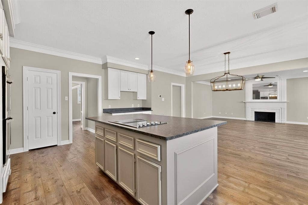 Kitchen island with integrated cooktop, pendant lighting, built-in ovens, wood-finish flooring, and a fireplace with a mantel
