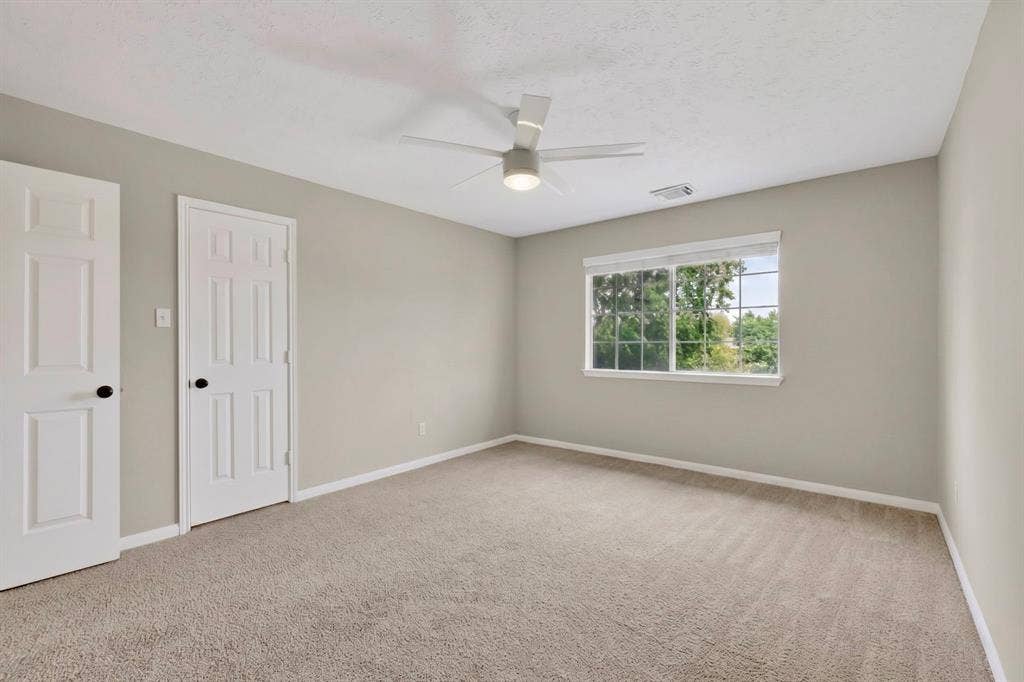 Neutral wall tones, carpet flooring, a ceiling fan with integrated lighting, and a single window
