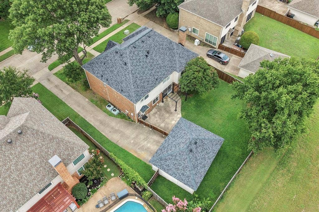 Expansive backyard featuring a manicured lawn, mature shade trees, and a detached structure with a shingle roof