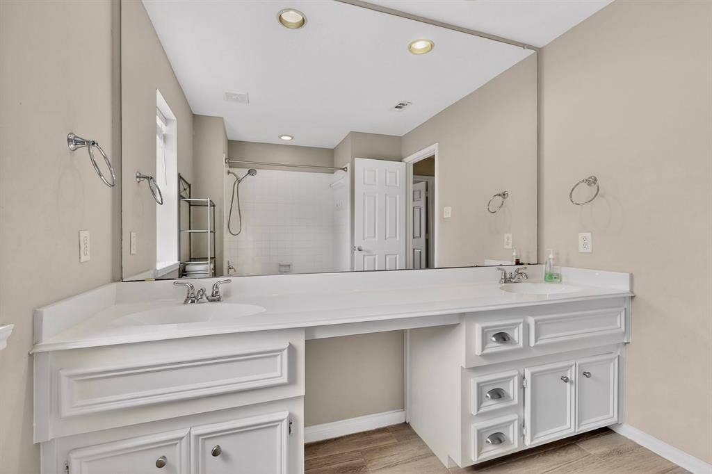 Dual vanity with white cabinetry, integrated sinks, chrome hardware, and a large wall-mounted mirror