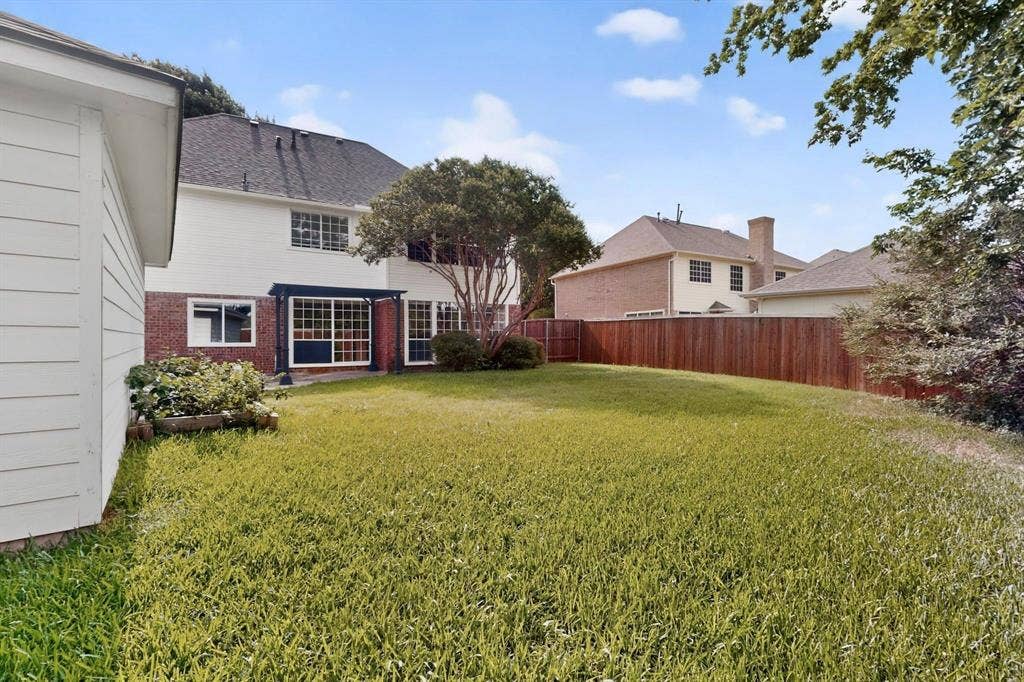 Expansive backyard with a manicured lawn, full privacy fencing, and a pergola-covered patio