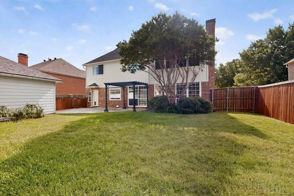 Expansive backyard featuring a concrete patio, a dark-toned pergola, and a privacy fence