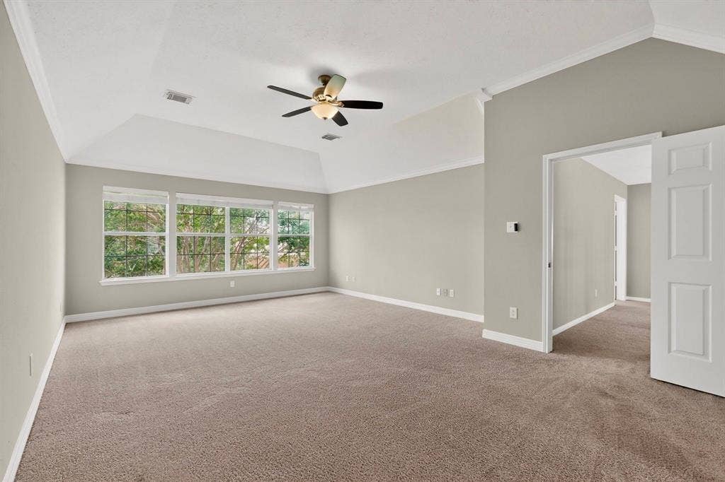 Spacious room featuring vaulted ceilings, a ceiling fan with integrated lighting, expansive windows with white trim, and neutral-toned carpeting