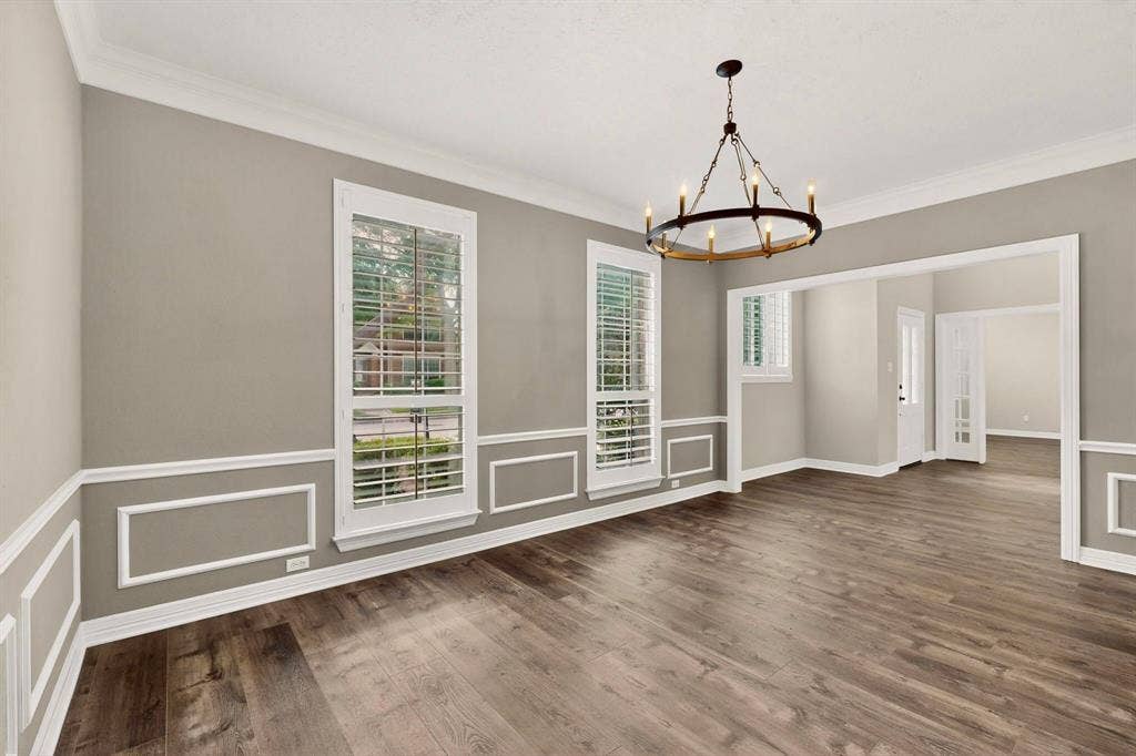Decorative wainscoting with crown molding, wood-finish flooring, and a chandelier with a dark bronze finish