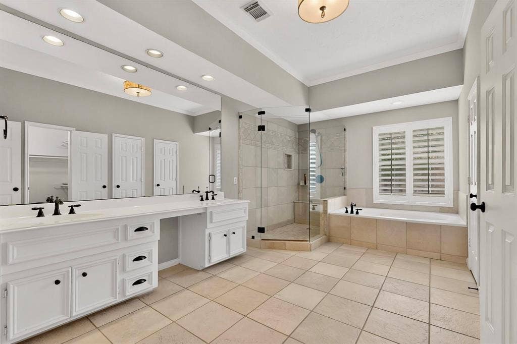 Dual vanity with integrated sinks, frameless glass shower enclosure, built-in soaking tub, plantation shutters, and large format tile flooring