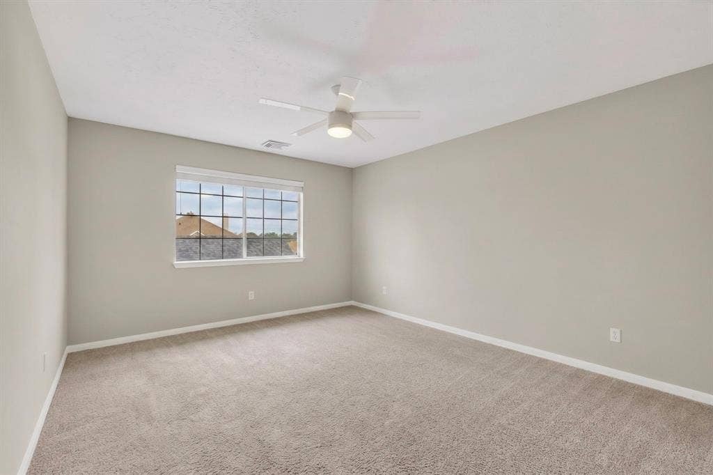 Spacious room with light-colored carpeting, a multi-pane window, and a ceiling fan with integrated lighting