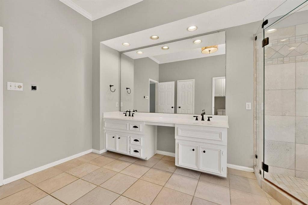 Dual vanity with white cabinetry and dark hardware, large wall-mounted mirror, recessed lighting, and a glass-enclosed shower with tile surround