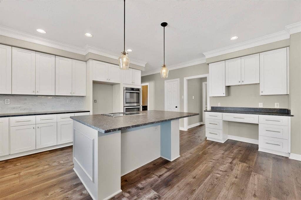 Spacious kitchen featuring white cabinetry, a large center island with dark countertops, wood-finish flooring, and recessed and pendant lighting