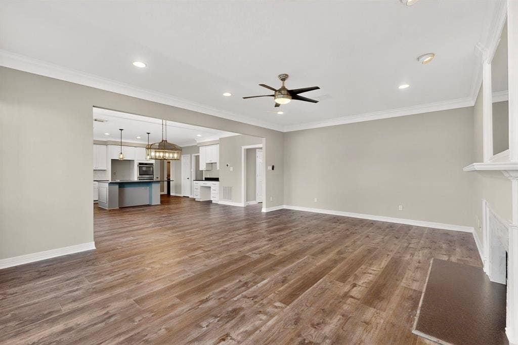 Wood-finish flooring, recessed lighting, crown molding, ceiling fan, and a built-in fireplace mantel