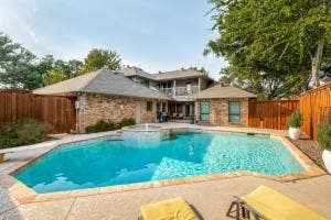 5212 Mustang Trail, Plano, TX 75093 Expansive backyard featuring a blue swimming pool, integrated spa with water feature, surrounding concrete patio, and a privacy fence