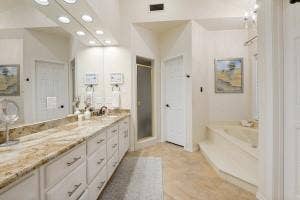 5212 Mustang Trail, Plano, TX 75093 Double vanity with light-toned countertop, extensive built-in cabinetry, large wall mirror, built-in bathtub, and enclosed shower