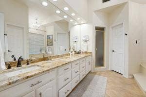 5212 Mustang Trail, Plano, TX 75093 Dual vanity with integrated sinks, expansive countertop, white cabinetry, large wall mirror, and a shower enclosure with a frosted glass door