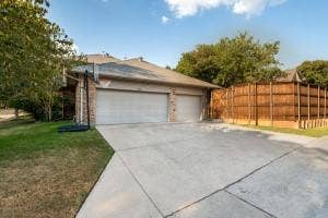5212 Mustang Trail, Plano, TX 75093 Two-car garage with overhead doors, brick facade, concrete driveway, and wood privacy fencing