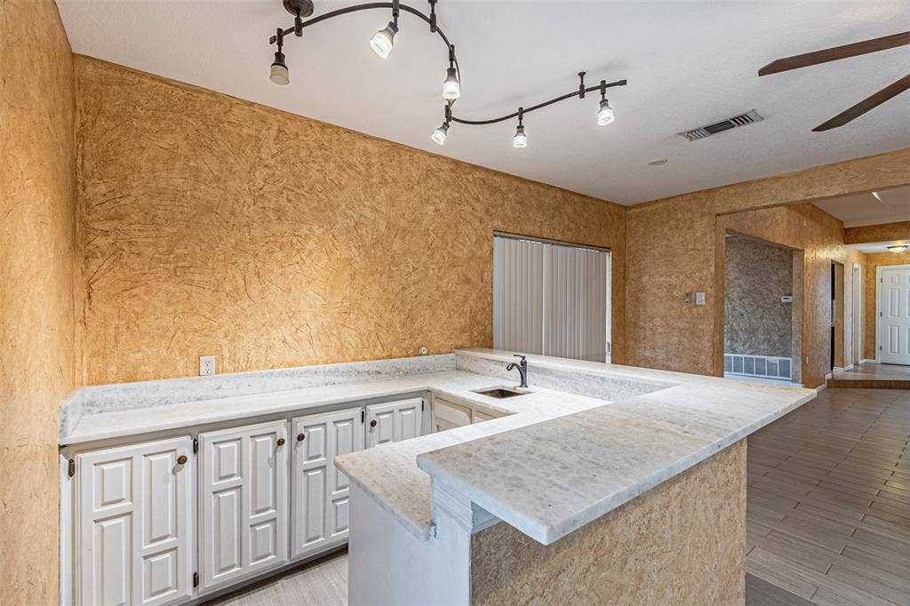 8808 Sylvan Court, Fort Worth, TX 76120 U-shaped counter with a built-in sink, track lighting, white paneled cabinetry, and wood-finish flooring